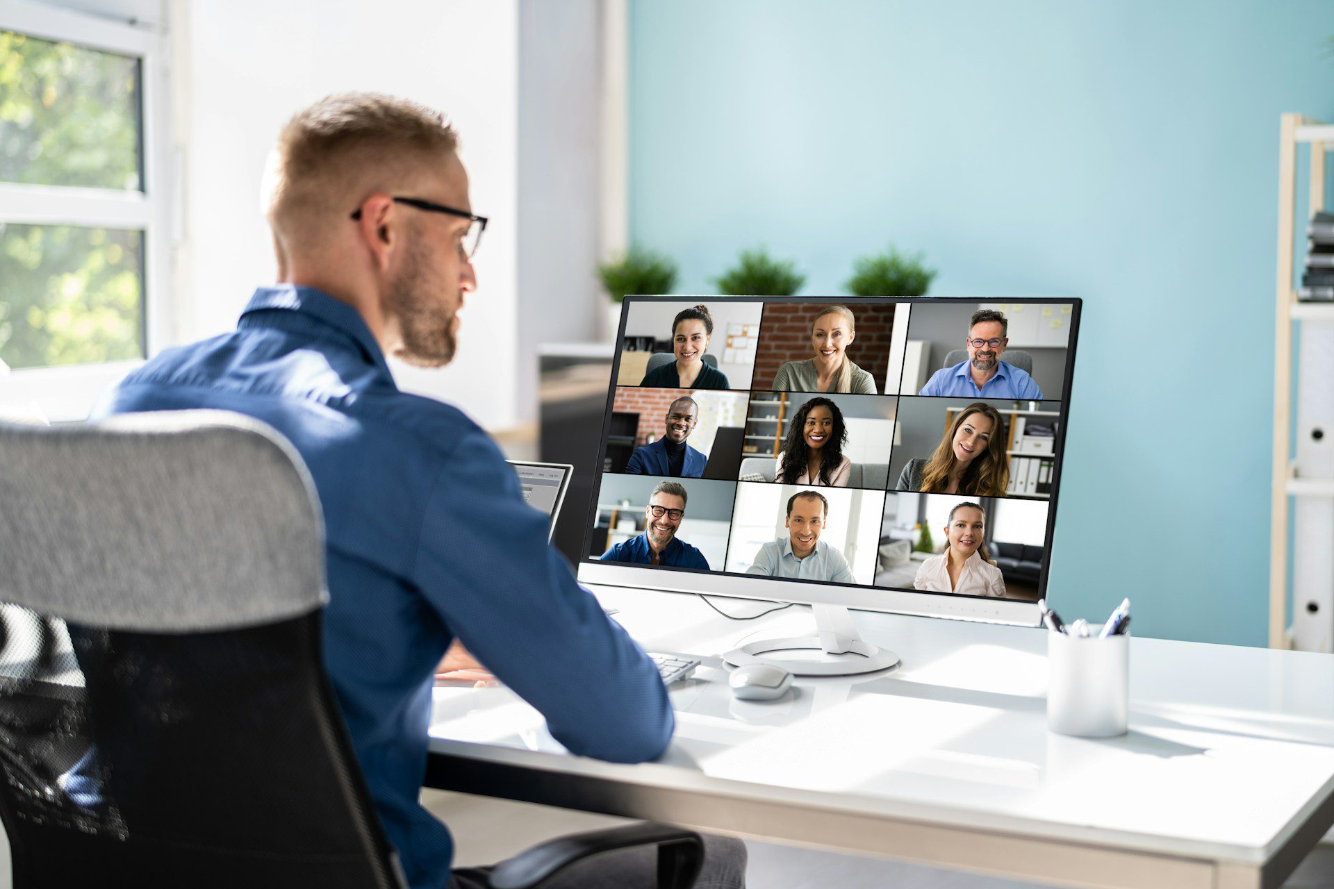 a remote employee on his computer with colleagues on the screen taking part in a virtual or hybrid corporate event